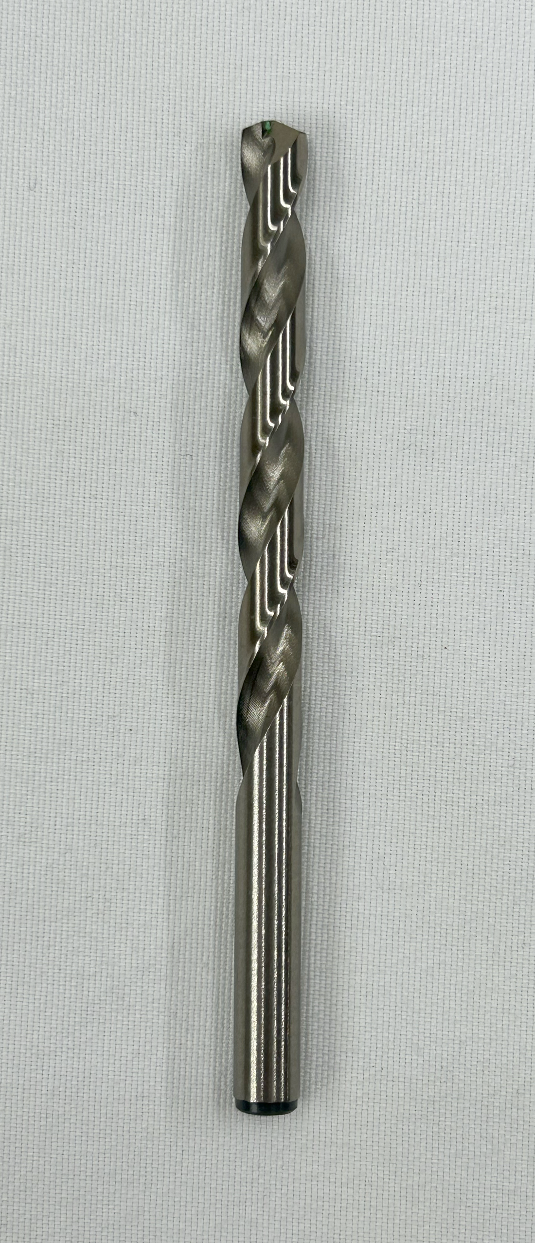 A single metal drill bit with a twisted flute design, shown vertically against a light gray textured background.