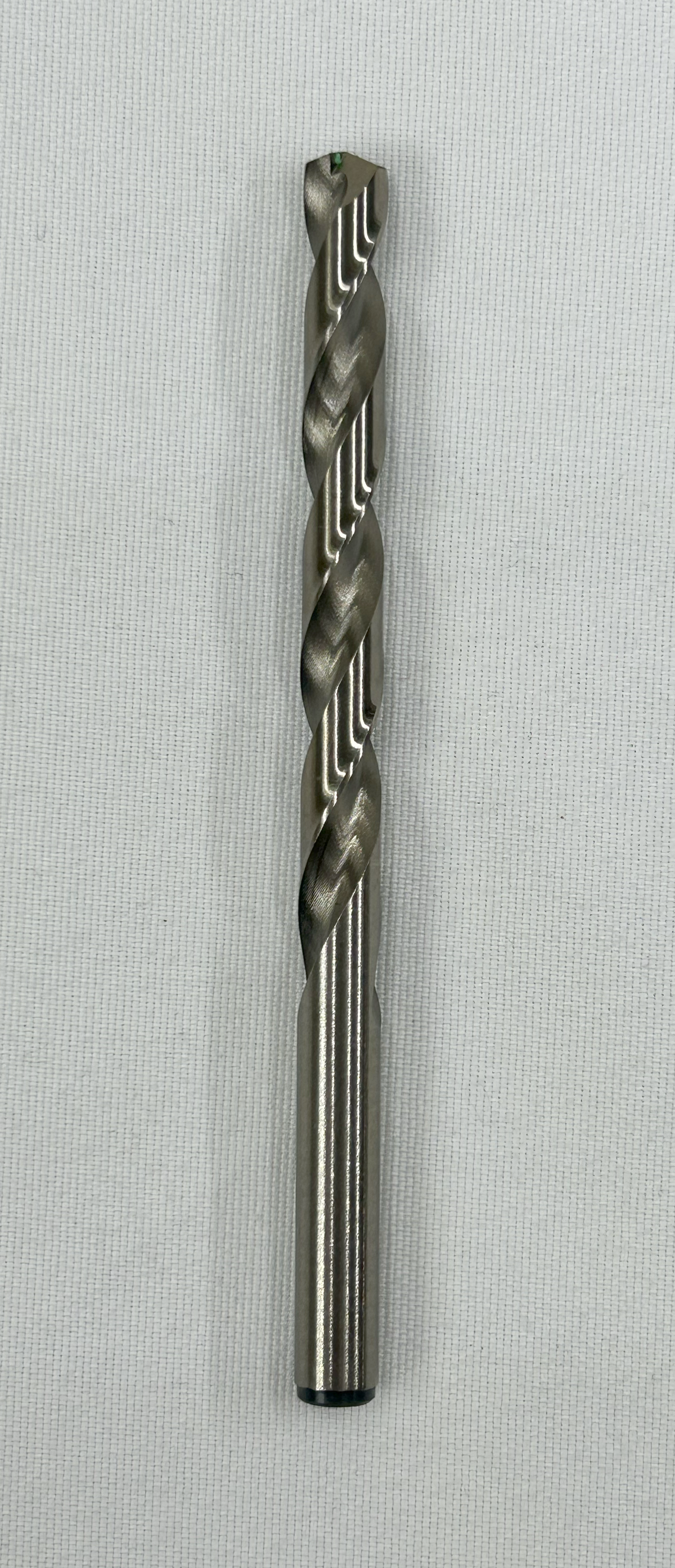 A single metal drill bit with a twisted flute design, shown vertically against a light gray textured background.