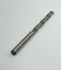A single metal drill bit with a dark protective tip, photographed diagonally on a textured white fabric background.