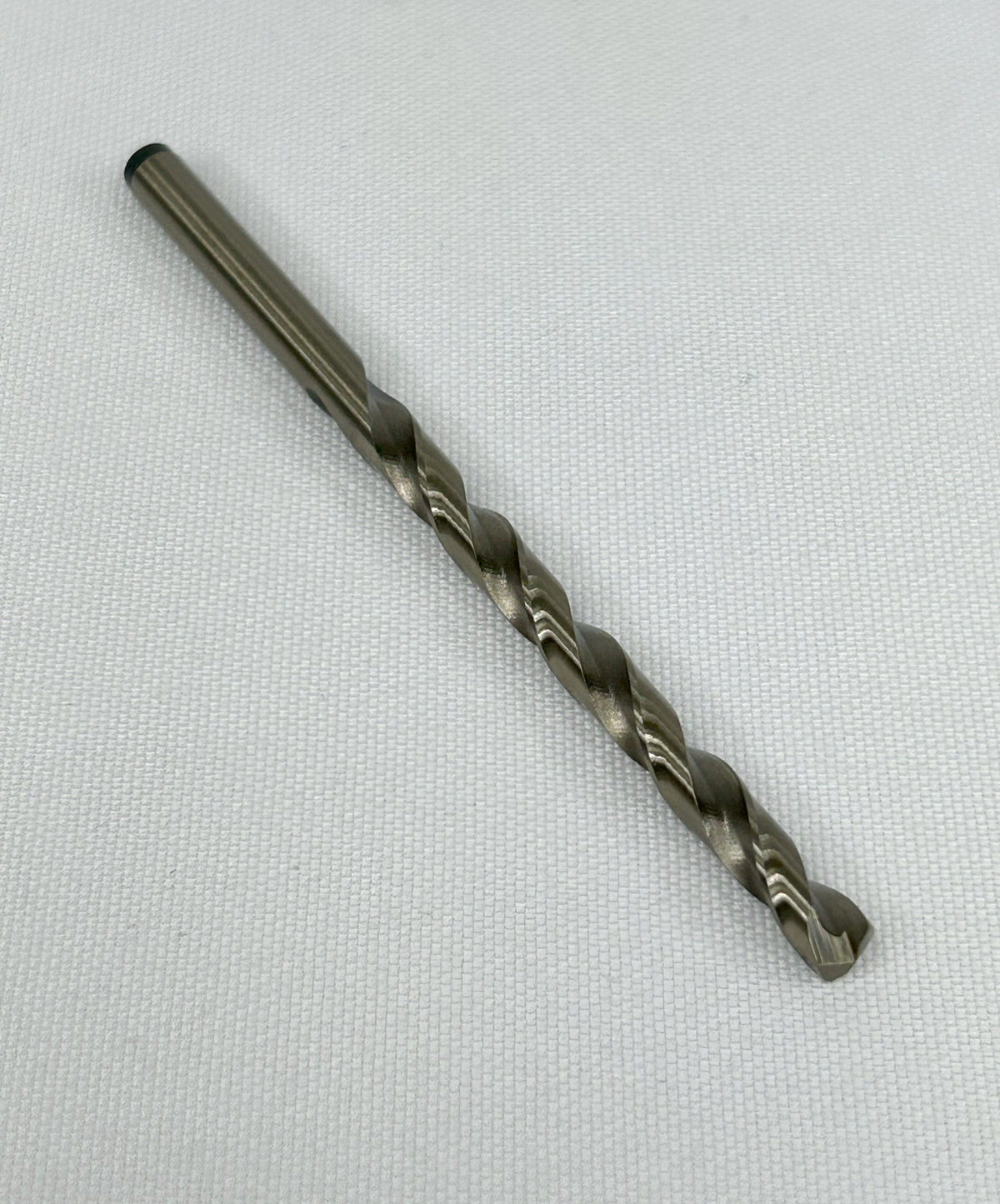 A single metal drill bit, wire size 7, with a fluted cutting shank, photographed diagonally on a textured white fabric background.