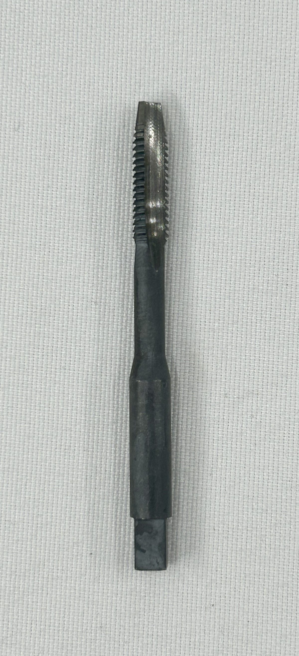 A dark metallic thread cutting tap tool with a square shank, shown vertically against a light gray textured background.