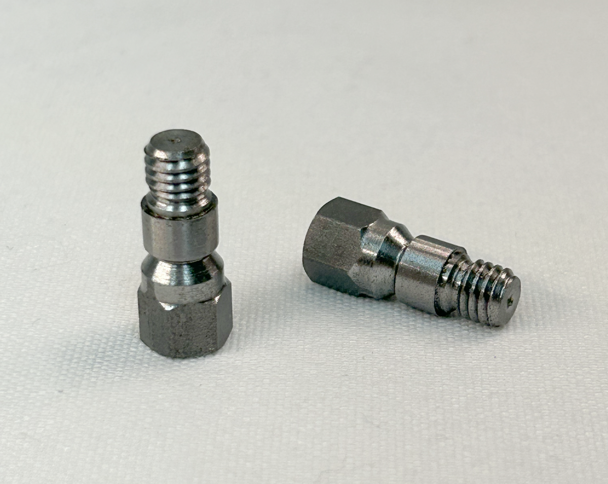 Two small metallic threaded adapter fittings on a light gray textured background.