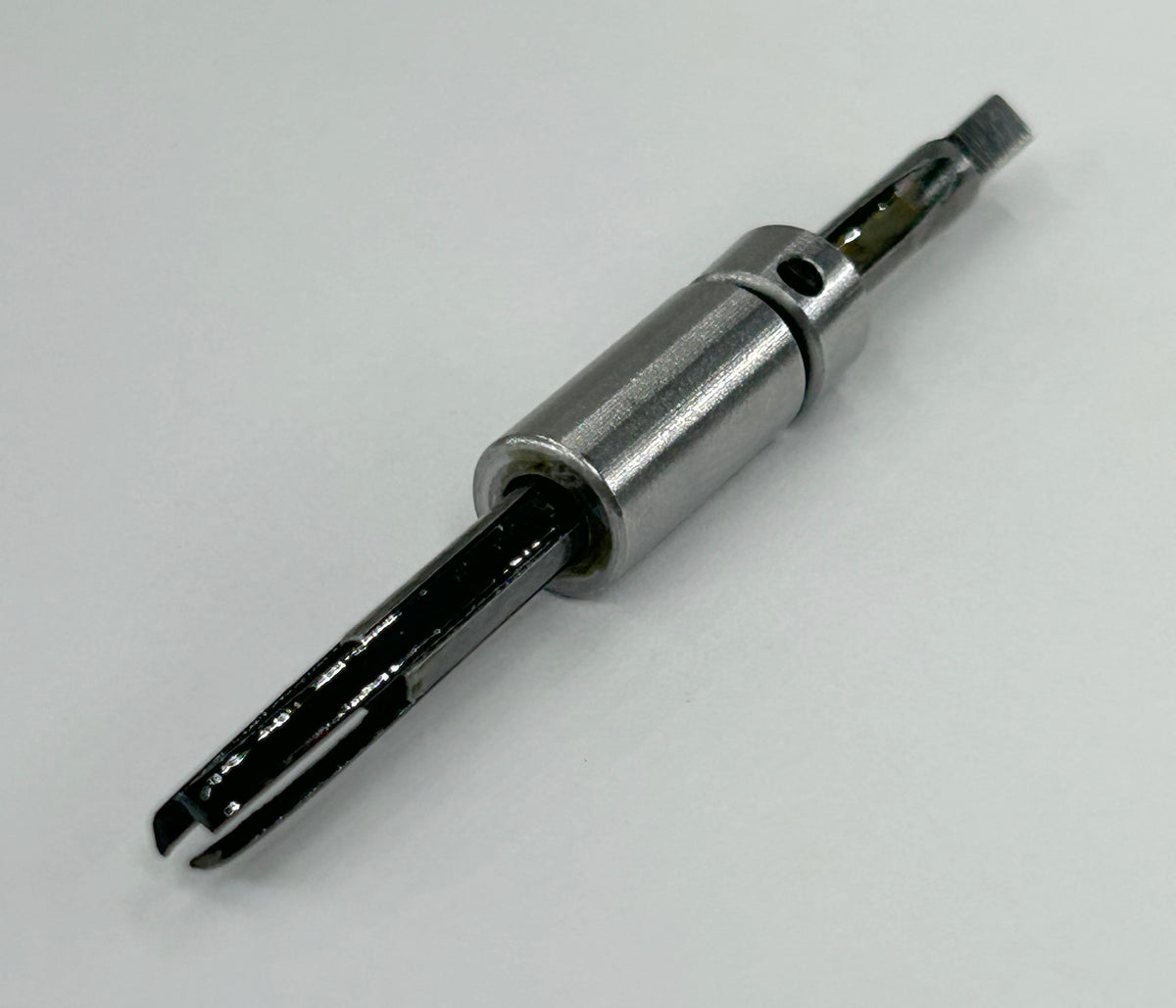 A close-up of a metallic cylindrical component with a black internal rod or sleeve, photographed on a plain light background.