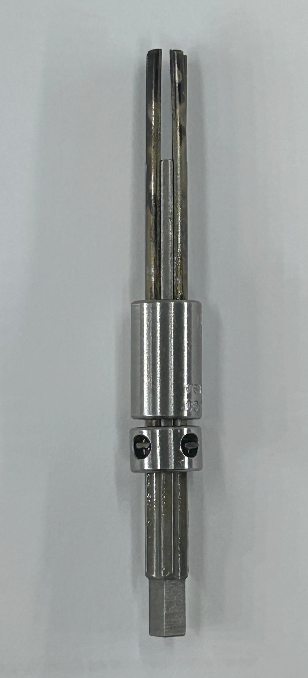 A metal rotary burr tool with a silver cylindrical body and two long fluted cutting bits extending upward, shown against a plain light gray background.